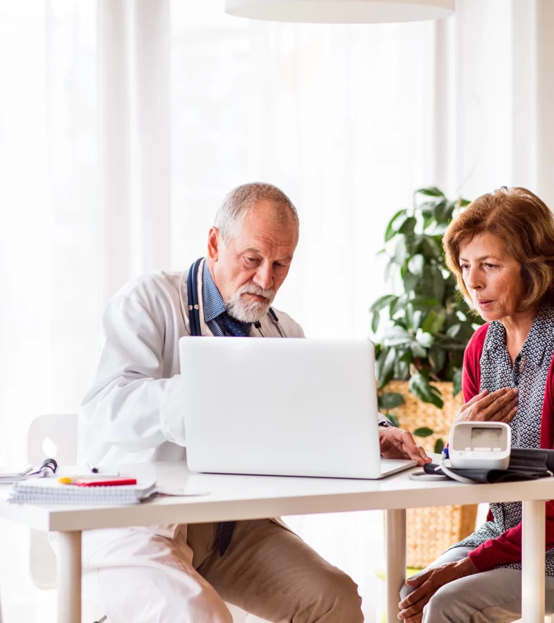 A doctor with a laptop talking to a senior woman in the office